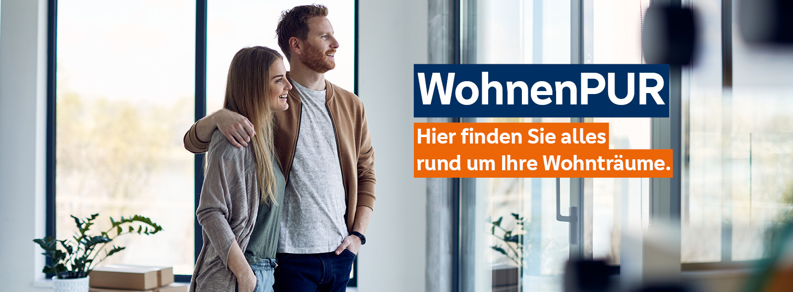 Junges glückliches Paar genießt den Ausblick durch das Fenster in ihrem neuen Zuhause.